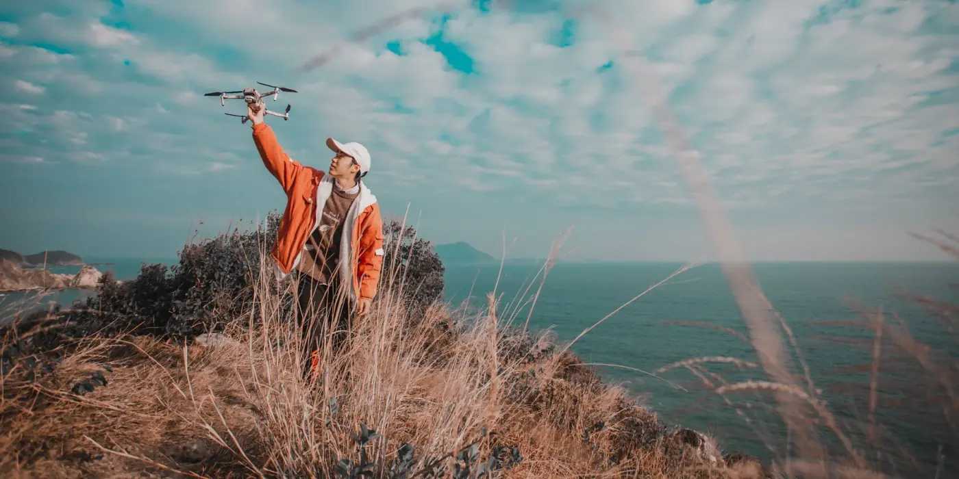 Pilot launching a DJI Mini drone from a coastal clifftop